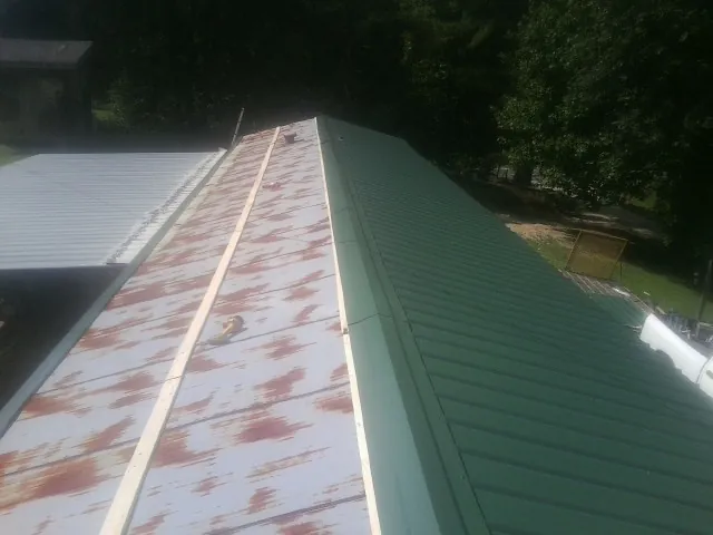 Old rusted panels beside newly installed green metal roofing — Wind Damage Roof Repair by Roofing Brothers in Billings