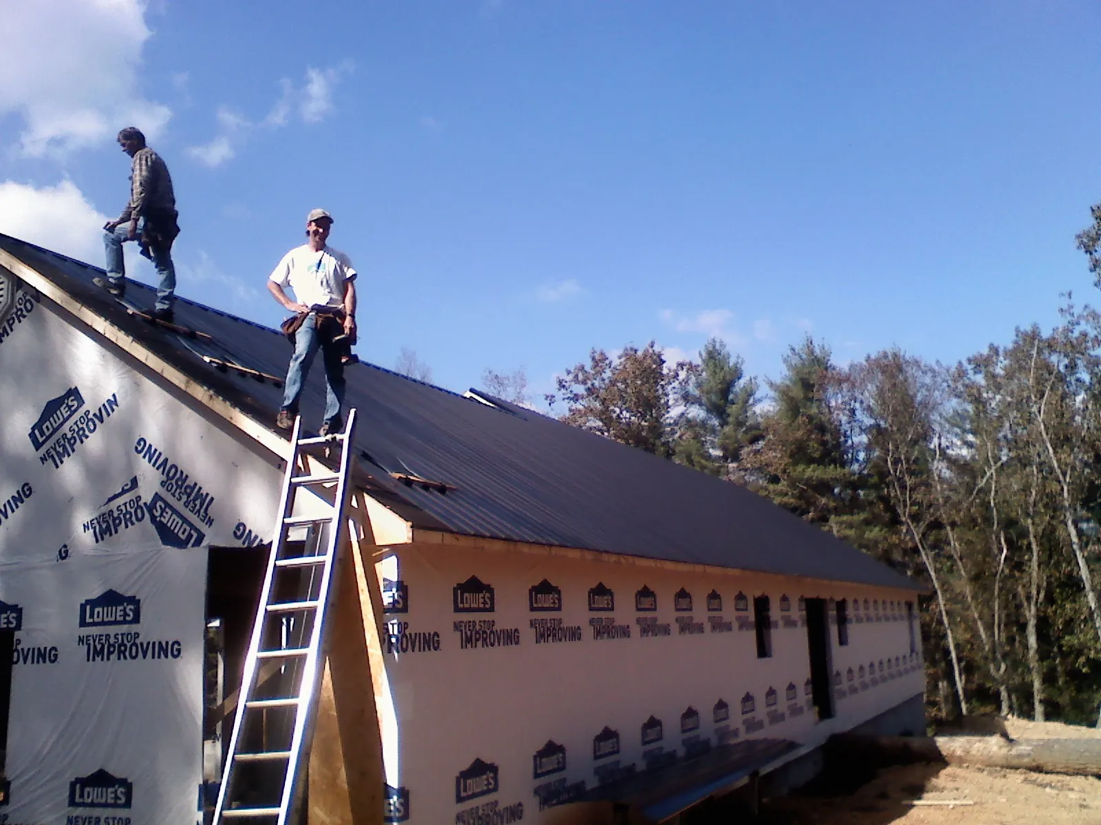 Two roofers standing on a long dark metal roof over a wrapped building in Billings